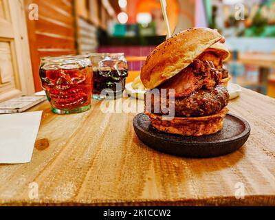 Beef Burger als hoher Turm mit Totenkopf-Gläsern für Getränke Stockfoto