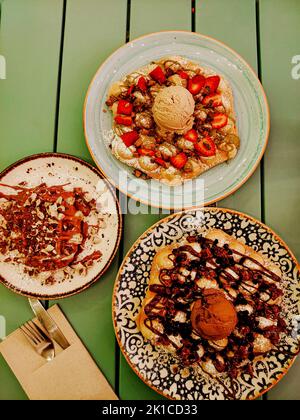 Blick von oben auf drei Waffelgerichte mit Eis, Schokolade und Erdbeeren auf einem Terrassentisch Stockfoto