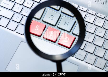 Lupe und Computertastatur mit Text „SEO“ auf roten Tasten Stockfoto