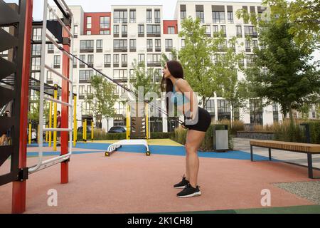 Profilaufnahme in voller Länge einer athletischen Frau, die mit einem Widerstandsband auf dem Straßen-Workout-Spielplatz trainiert Stockfoto