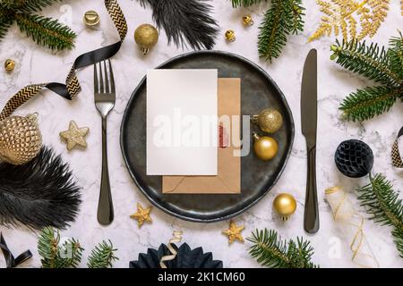 Schwarz-goldenes Tischgedeck mit Ornamenten und Tannenzweigen, Draufsicht, Einladungskarte Mockup. Stimmungsvolle Komposition zu Weihnachten oder Neujahr Stockfoto