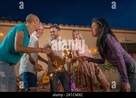 Eine Gruppe reifer Freunde feiert mit Funkeln auf einer privaten Party im Hinterhof oder in einem Club. Fröhliche und fröhliche Menschen feiern in einem Nachtclub Stockfoto