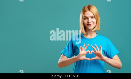 Unterstützende Frau. Liebe Fürsorge. Fröhliche Dame in blauem T-Shirt zeigt Herz Geste isoliert auf teal Kopie Raum Werbung Hintergrund. Romantische Botschaft. Stockfoto