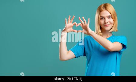 Liebeszeichen. Mitgefühl. Enthusiastisch dankbare Frau in blauem T-Shirt zeigt Herzgesten isoliert auf blauem leeren Raum kommerziellen Hintergrund. Stockfoto