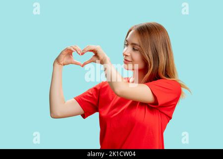 Dankes-Zeichen. Liebe Zuneigung. Porträt einer unterstützenden, freundlichen Frau im roten T-Shirt mit einer isolierten Herzbewegung auf blauem Hintergrund. Romantisches Chaos Stockfoto