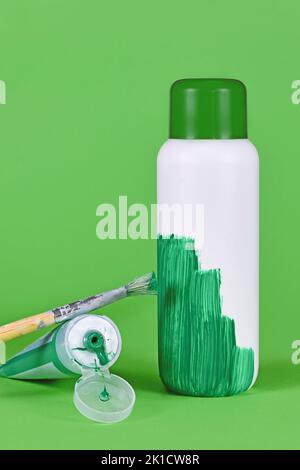 Greenwashing-Konzept mit weißer Plastikflasche, die grün lackiert wird Stockfoto