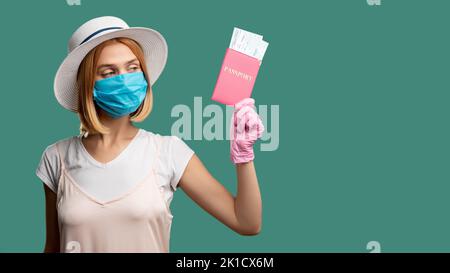 Quarantänemaßnahmen. Reisebüro. Frau im Sommer Outfit Schutzmaske rosa Handschuhe Blick auf ausländische id mit Tickets isoliert auf grünen Kopieplatz Stockfoto