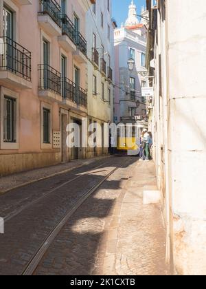 Lissabon, Portugal, 24. Oktober 2021: Blick auf die steile, schmale Lissabonner Straße mit der typischen gelben Straßenbahn der Linie 28, Ikone und Symbol der Stockfoto