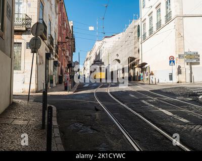 Lissabon, Portugal, 24. Oktober 2021: Blick auf die steile, schmale Lissabonner Straße mit der typischen gelben Straßenbahn der Linie 28, Ikone und Symbol der Stockfoto