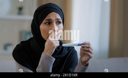 Schockiert unglücklich islamische junge Frau arabisch muslimische Mädchen in Hijab weiblichen Erwachsenen schwanger Gefühl Angst Blick auf positive Schwangerschaftstest Ergebnis sitzen an Stockfoto