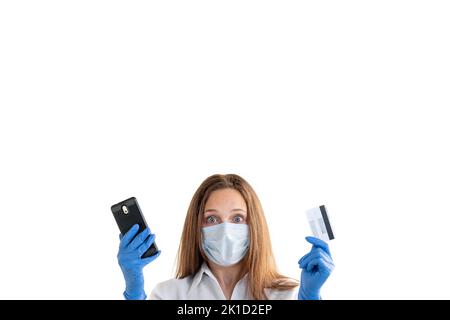 Bankprobleme. Covid-19-Beschränkung. Gesperrtes Konto. Online-Zahler. Schockierte Frau in Schutzmaske Handschuhe halten Kreditkarte und Handy-Look Stockfoto