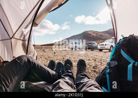 Die Beine eines Paares, das sich im Sommer in Island in einem Zelt in der Wildnis auf dem Campingplatz entspannt Stockfoto