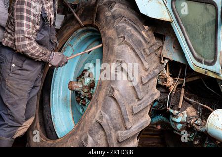 Wechseln Sie zu Hause den beschädigten Schlauchreifen des landwirtschaftlichen Traktors. Ein Arbeiter benutzt Brechstangen, um unter den Rand des Randes zu hebeln und die Perle zu brechen. Stockfoto