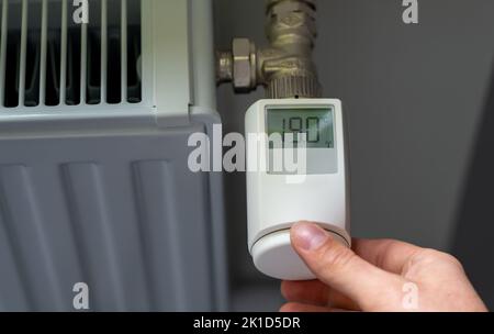 Hand dreht die Temperatur auf 19 Grad Celsius auf einem elektronischen Thermostat. Symbol für Energieeinsparung. Stockfoto