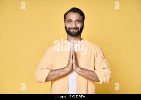 Achtsamer, glücklicher indischer Mann meditiert und hält Hände in Namaste isoliert auf Gelb. Stockfoto