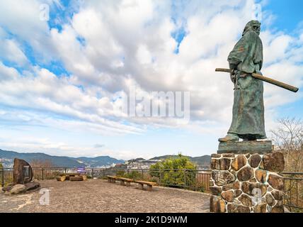 nagasaki, kyushu - 14 2021. dezember: Statue des japanischen Samurai Sakamoto Ryōma mit einem Kimono und Katana-Schwertern, die vor Bänken und stehen Stockfoto