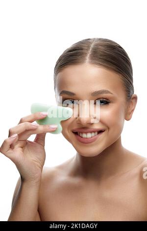 Frau mit Schönheitsgesicht mit Gesichtsbehandlung Gua Sha. Schöne lächelnde Mädchen tun Gesichtsmassage. Spa.Hautpflege. Stockfoto