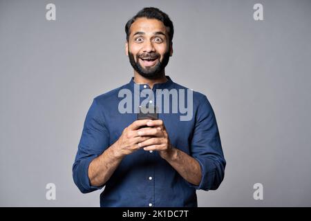 Aufgeregt indischen Geschäftsmann mit Mobiltelefon isoliert auf grauem Hintergrund. Stockfoto