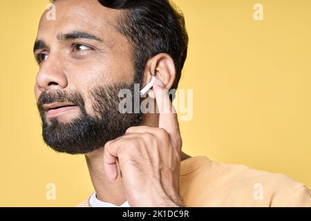 Lächelnder indischer Mann mit Ohrhörern, der Musik oder Podcast hört. Nahaufnahme Stockfoto