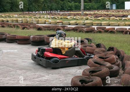 Kartsport. Go Kart auf der Strecke. Junge positive Rennfahrer, die während eines Autorennens auf einer Autorennbahn im Freien einen Kart fahren. Extremer Motorsport. Stockfoto