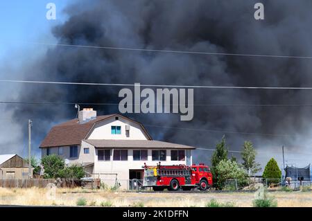 Feuerwehrauto am Ort eines Hausfeuers mit riesigen Wolken wehenden Rauchs, die den Himmel füllen. Stockfoto