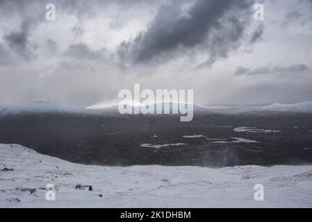 Wunderschöne Winterlandschaft von der Bergspitze in den schottischen Highlands hinunter in Richtung Rannoch Moor während Schneesturm und Spindrift von der Bergspitze hinein Stockfoto