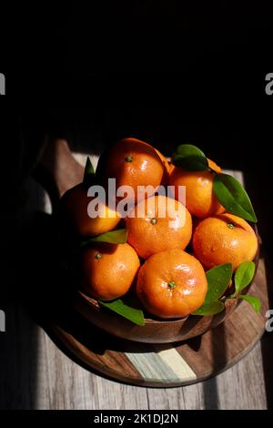 Nahaufnahme von Mandarinen mit Blättern in einer Holzschale, Draufsicht Stockfoto