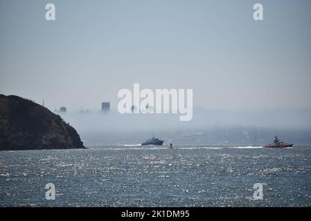 Ein wunderbarer großformatiger Panoramablick auf San Francisco im dichten Nebel von der anderen Seite der glitzernden Bucht, mit Kreuzfahrtbooten im Vordergrund. Stockfoto