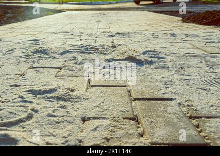 Pflasterplatten aus Kunststein in der Phase der Füllung der Fugen mit trockenem gesiebtem Sand, selektiver Fokus Stockfoto