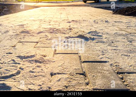 Pflasterplatten aus Kunststein in der Phase der Füllung der Fugen mit trockenem gesiebtem Sand, selektivem Fokus und Hintergrundbeleuchtung Stockfoto