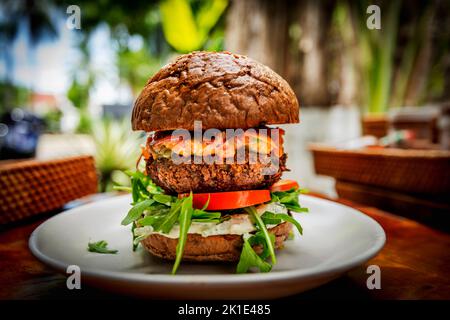 Veganer Burger auf einem Brötchen auf einem weißen Teller mit Tomate, spezieller Sauce, Rucola. Stockfoto