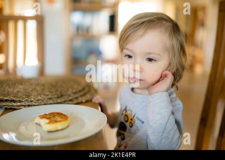 Niedlicher kleiner Kleinkind Junge, der zu Hause Pfannkuchen isst. Frische Bio-Lebensmittel für Kleinkinder. Gesunde Ernährung für Familien mit Kindern. Stockfoto