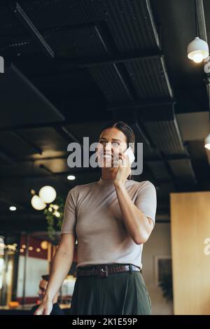 Geschäftsfrau, die einen Anruf in einem Co-Working-Raum entgegennimmt. Glückliche junge Geschäftsfrau lächelt, während sie mit ihren Kunden kommuniziert. Unternehmerin W Stockfoto