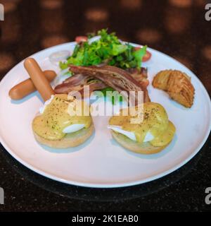 Egg benedict auf einem Teller mit Salat und Wurst und Hollandaise-Sauce isoliert Stockfoto