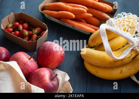 Verschiedene Gemüse und Früchte in wiederverwendbaren Verpackungen aus Papier und Stoff auf einem blauen Holztisch. Umweltfreundliches Verpackungskonzept. Draufsicht. Stockfoto