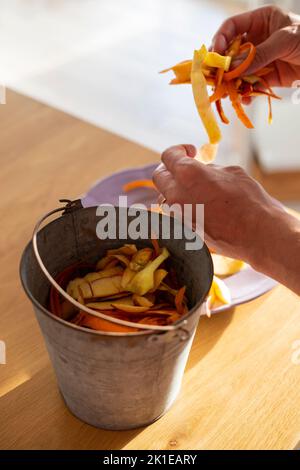 Männliche Hände sortieren Gemüseschälchen in Zinnbehälter. Verwendung von Lebensmittelabfällen, Kompostierung, um die Bodenfruchtbarkeit zu bereichern. Mülltrennung zu Hause. Vertikal Stockfoto