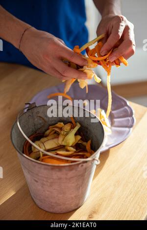 Männliche Hände sortieren Gemüseschälchen in Zinnbehälter. Verwendung von Lebensmittelabfällen, Kompostierung, um die Bodenfruchtbarkeit zu bereichern. Mülltrennung zu Hause. Vertikal Stockfoto