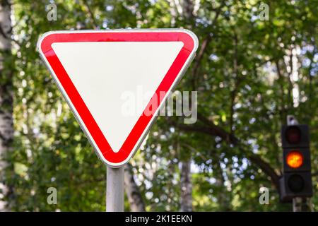 Das russische Straßenschild räumt dem Verkehr auf der Hauptstraße vor uns Priorität ein. Wegweiser mit Bäumen und Ampel im Hintergrund verwischen.Gefahrenwarnung und sto Stockfoto