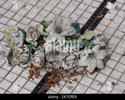 Ein Strauß alter grauverwitterter Plastikblumen auf kleinen weißen Fliesen Stockfoto