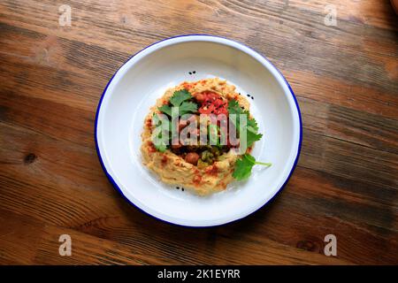 Hummus mit Kichererbsen auf weißem Teller auf Holztisch. Draufsicht, flach. Stockfoto