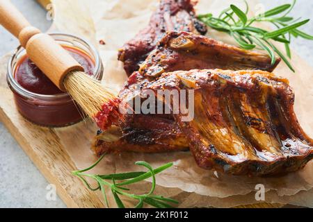 Gegrillte und geräucherte Schweinerippen mit Grillsauce auf einem alten Holzschneidebrett auf altem Holztisch-Hintergrund. Leckerer Snack bis Bier. Amerikanisch Stockfoto