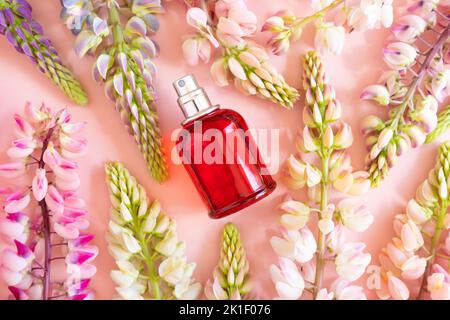 Parfümspray rote Flasche und rosa Lupinenblüten auf rosa Hintergrund. Vorderansicht oben, Sommerflachlage, Mockup. Stockfoto