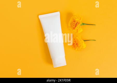 Mockup weiße Squeeze-Flasche Kosmetikschlauch und Ringelblumen auf gelbem Hintergrund. Feuchtigkeitscreme сream, Gleitgel, Hautpflege, Sonnencreme. Flache Lay, Stockfoto