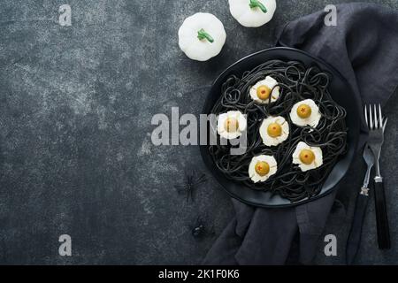 Halloween Party italienische schwarze Pasta dekoriert Horror Oliven wie Augen auf schwarzem Teller auf alten dunklen Tisch Hintergrund. Monster Gesicht von Pasta. Halloween Stockfoto