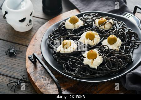 Halloween Party italienische schwarze Pasta dekoriert Horror Oliven wie Augen auf schwarzem Teller auf alten dunklen Tisch Hintergrund. Monster Gesicht von Pasta. Halloween Stockfoto