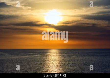 Atemberaubenden Sonnenuntergang in einem dramatischen Himmel über eine heitere, ruhige Meer Stockfoto