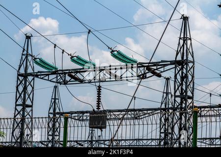 Stahlmasten, die Hochspannungsleitungen für Energiezwecke unterstützen, klarer blauer Himmel mit wenigen Wolken Stockfoto