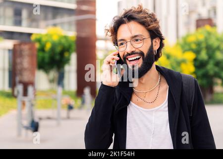 Lächelnder junger Mann, der glücklich in der Stadt telefoniert Stockfoto