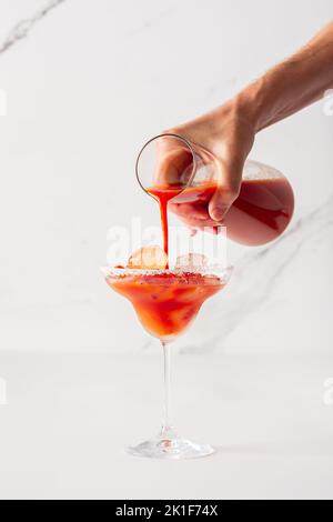 Ein Mann gießt ein alkoholisches Getränk mit Tomatensaft in ein Glas mit Eis Stockfoto