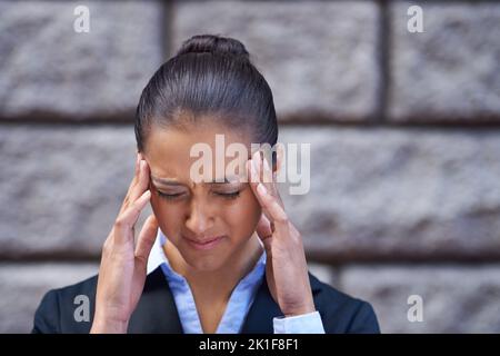 Unter Druck. Eine gestresste junge Geschäftsfrau mit den Händen auf den Schläfen. Stockfoto